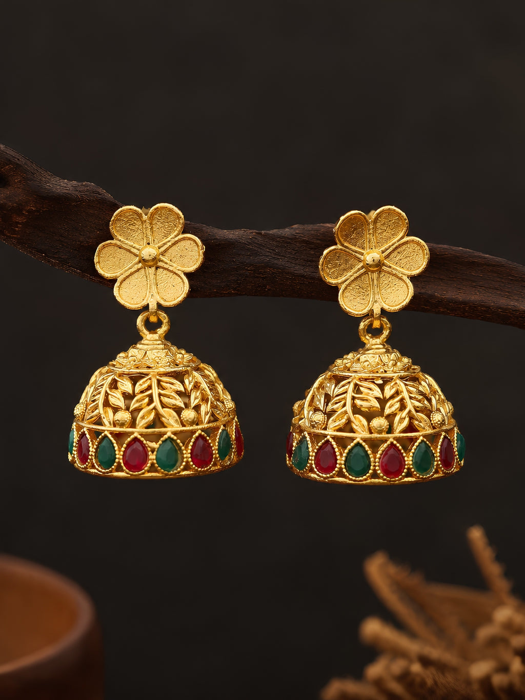 Gold earrings with floral design and colored stones on a dark background
