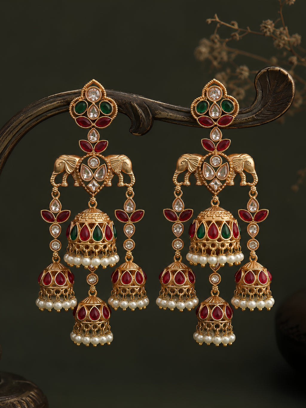 Ornate gold earrings with red and green gemstones on a dark background