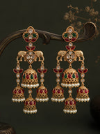 Ornate gold earrings with red and green gemstones on a dark background