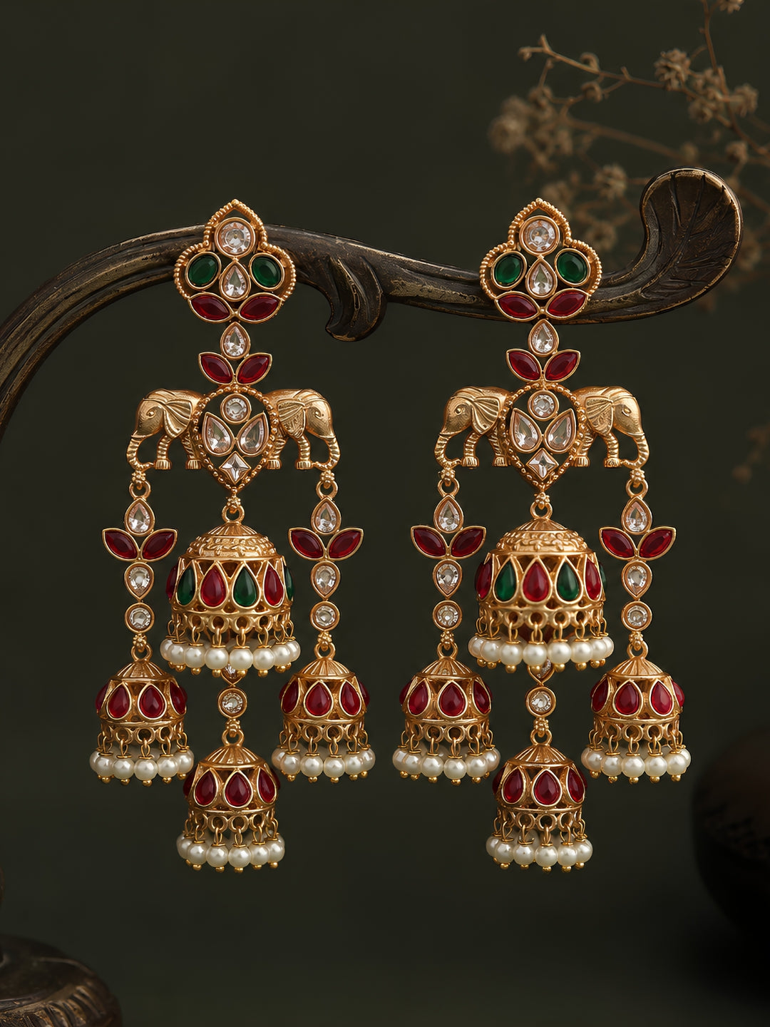 Ornate gold earrings with red and green gemstones on a dark background