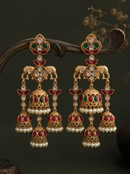 Ornate gold earrings with red and green gemstones on a dark background