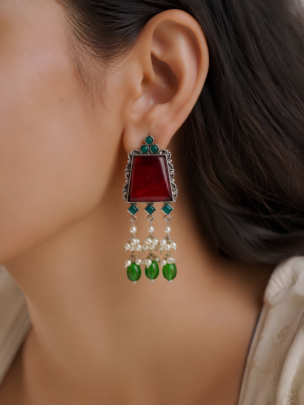 Close-up of an earring with red stone, green and blue beads, and pearl-like elements.
