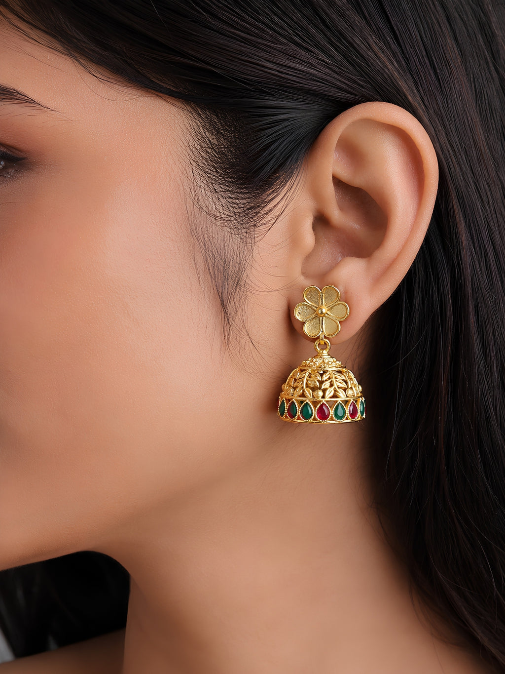 Gold earring with floral design and gemstones worn by a person