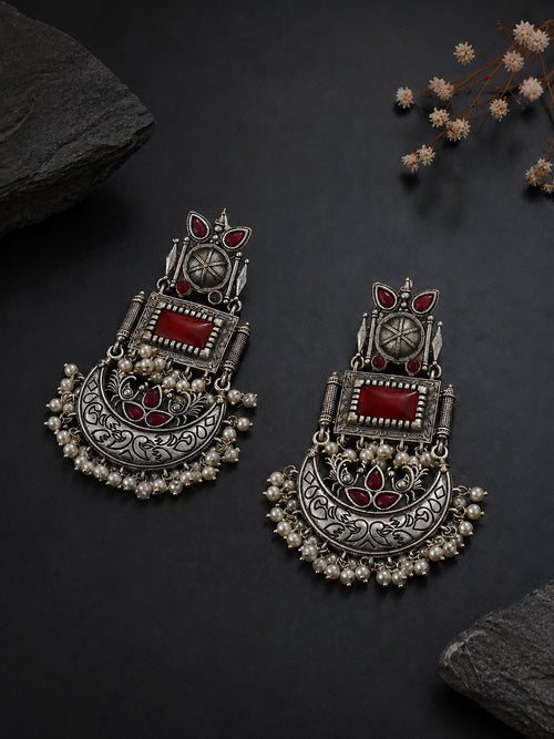 Ornate silver earrings with red stones on a dark surface
