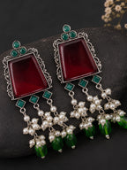 Ornate earrings with red stones, pearls, and green beads on a dark surface.