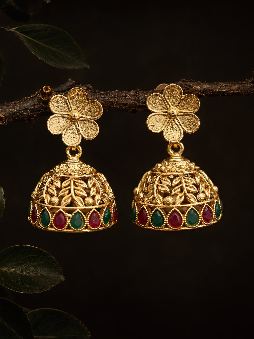 Gold floral earrings with red and green gemstones on a dark background
