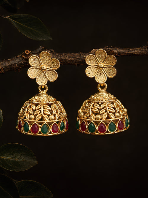 Gold floral earrings with red and green gemstones on a dark background