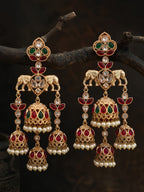 Ornate gold earrings with red and green gemstones on a dark background