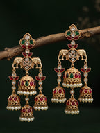 Ornate gold earrings with red and green gemstones on a dark background
