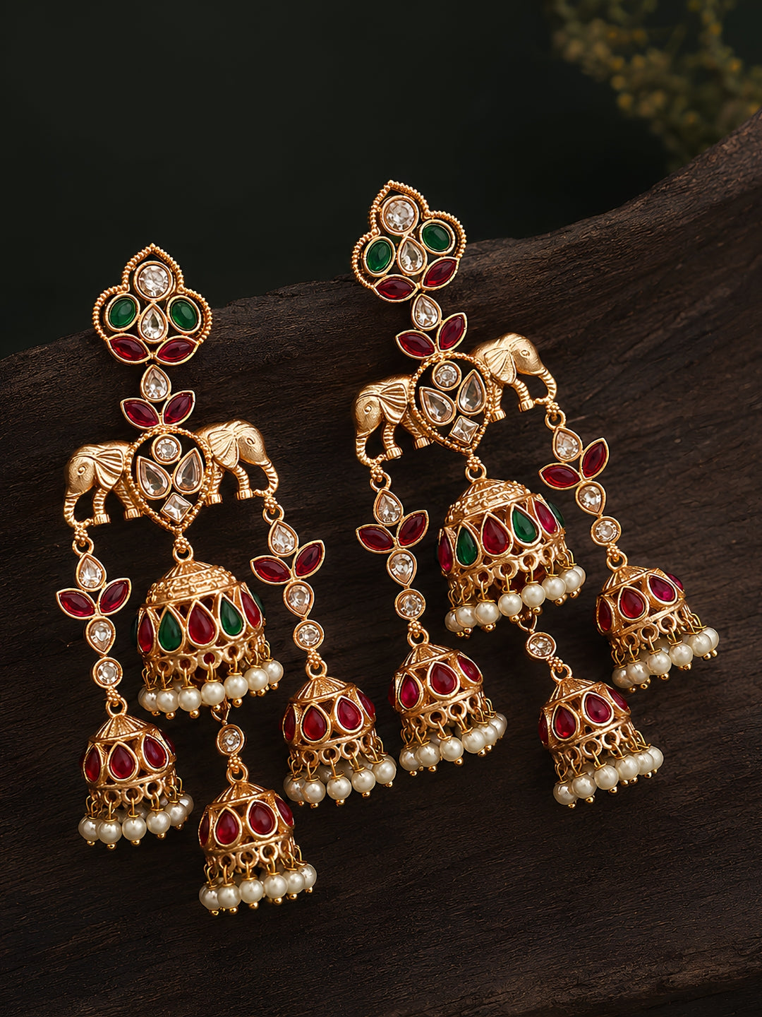 Ornate gold earrings with red, green, and pearl accents on a dark surface