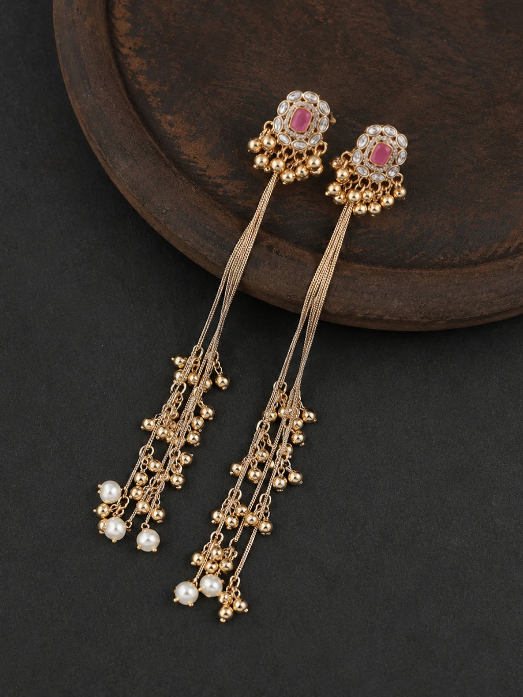 Gold earrings with pink gemstones on a dark surface, Kashmiri Jhumka