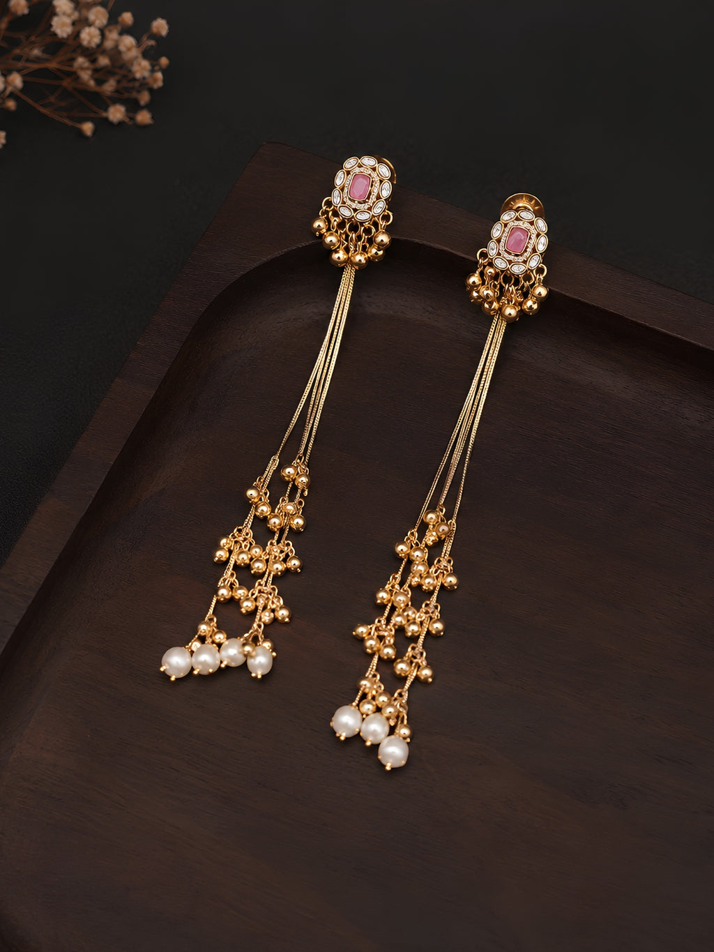 Gold earrings with pink gemstones and pearl drops on a dark background