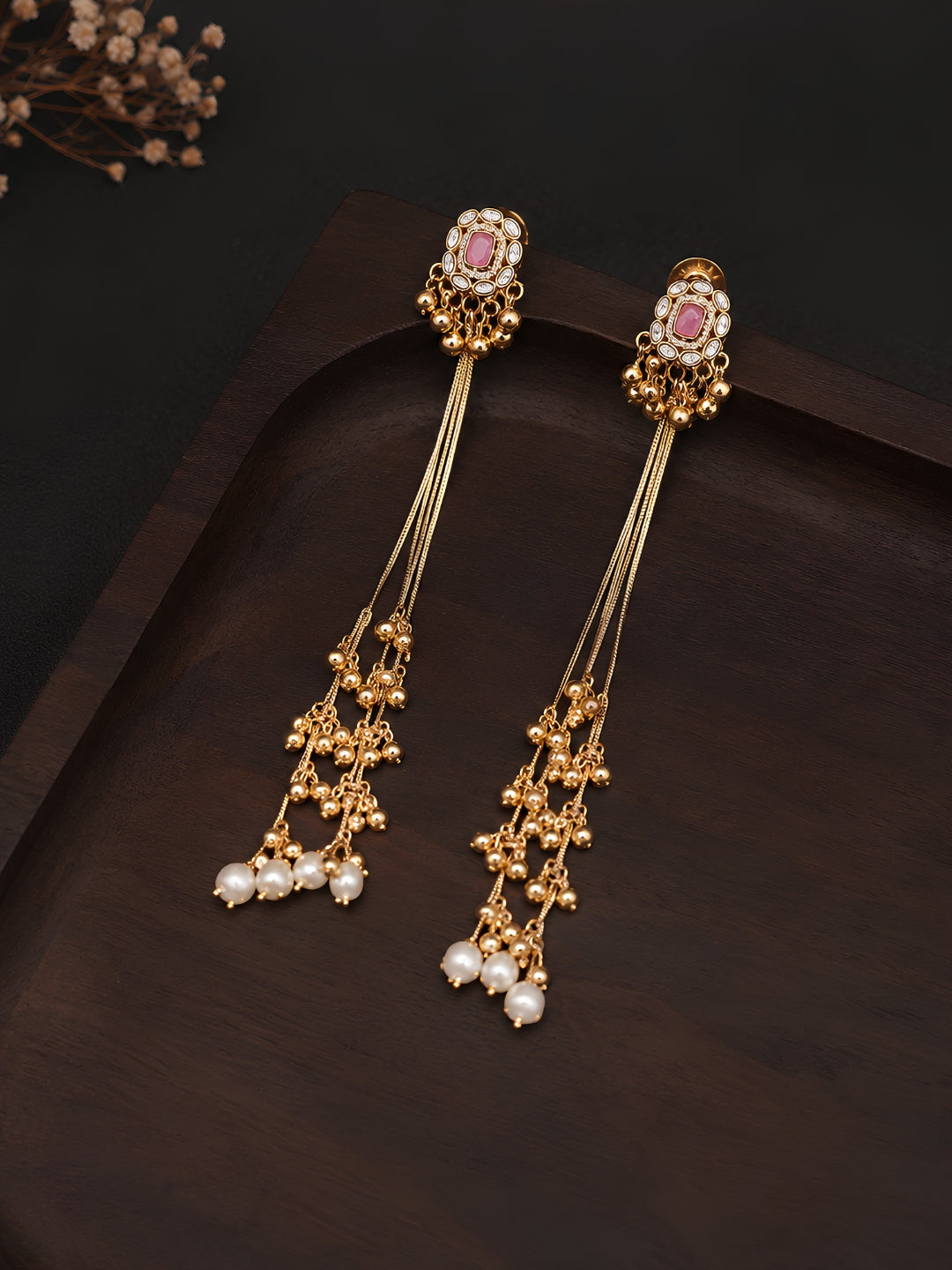Gold earrings with pink gemstones and pearl drops on a dark background