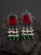 Pair of earrings with red stones, green beads, and pearl-like elements on a dark rock background.