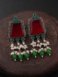 Pair of earrings with red stones, green beads, and pearl-like elements on a dark background