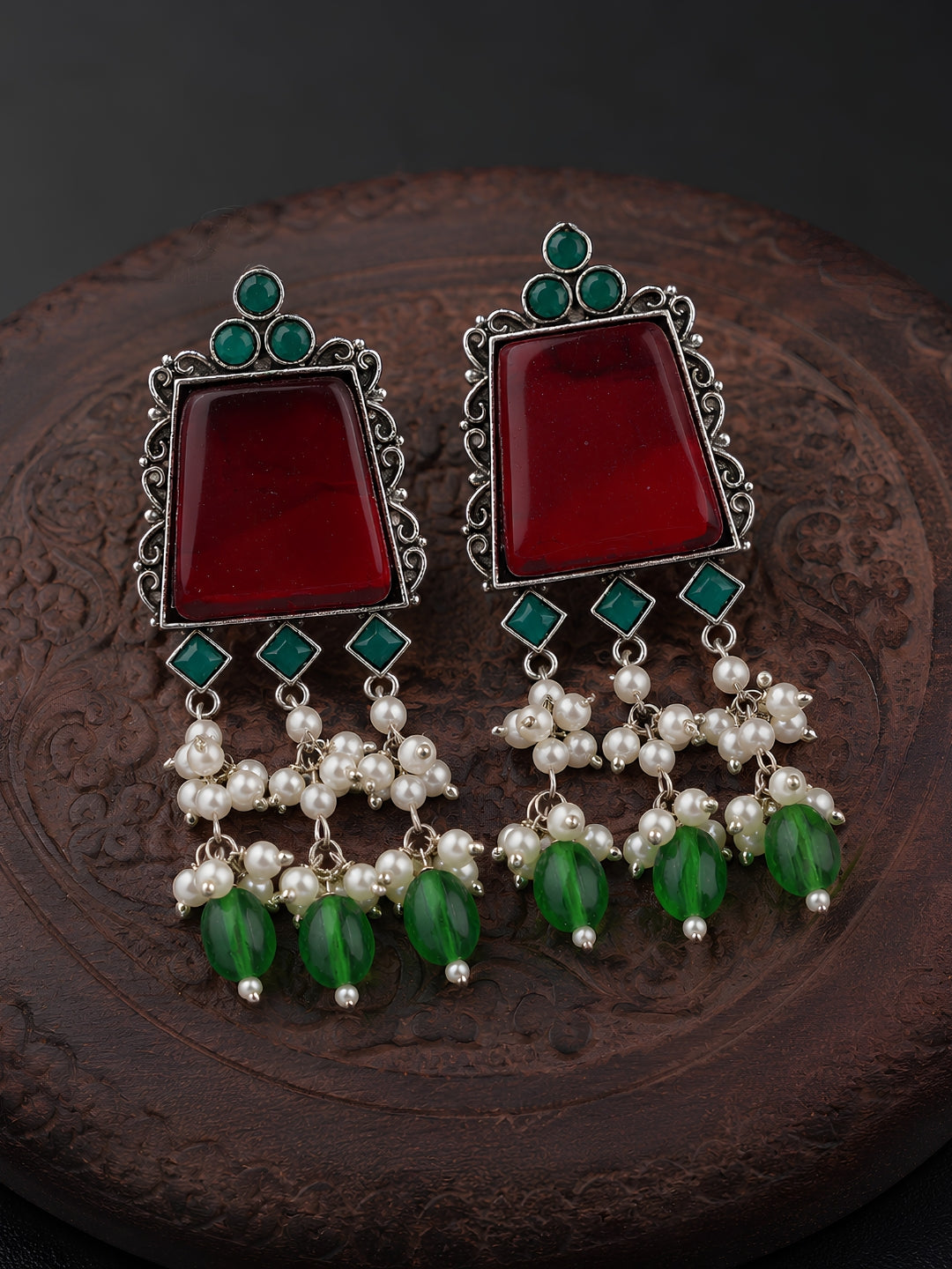 Pair of earrings with red stones, green beads, and pearl-like elements on a dark background